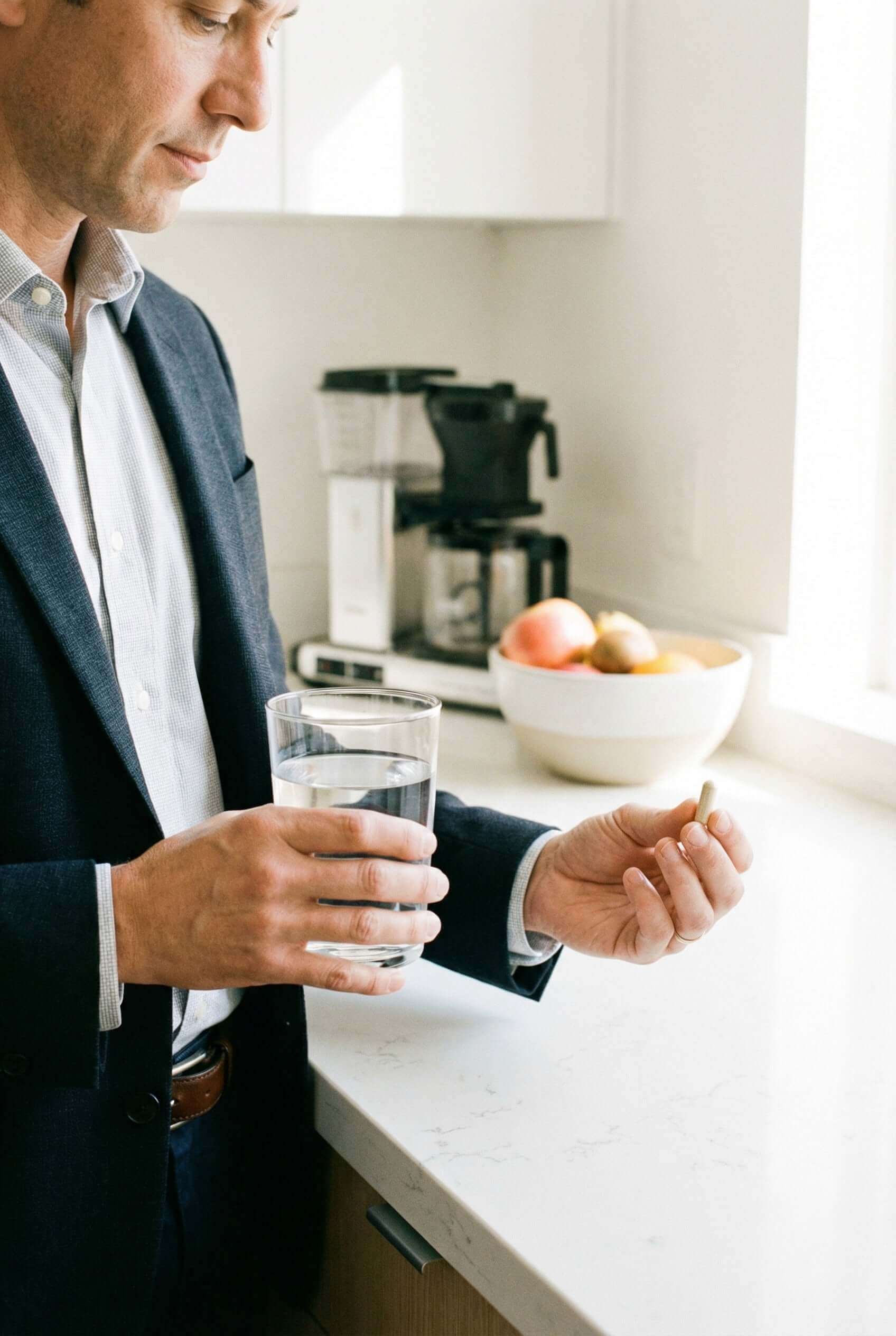 Pleniage NR NAD+ Nicotinamina ribosido - dosis optimizada. Hombre en cocina tomando una capsula con un vaso de agua